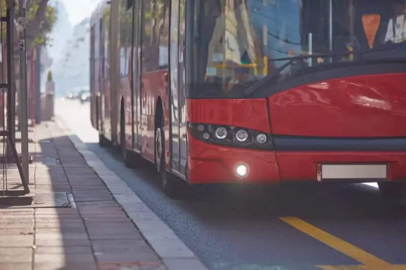 Red bus driving on road next to curb by bus stop